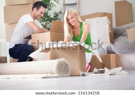 Happy Young Couple Unpacking Or Packing Boxes And Moving Into A New Home.