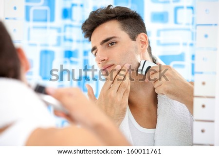 Young man shaving by electric shaver