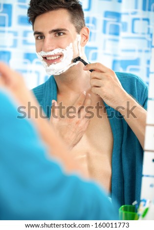 Young man shaving with a razor blade and shaving cream in bathroom