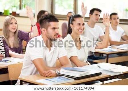 Students In Classroom Answering On Questions With Raised Hands