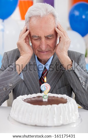 Senior man looking at  birthday cake thoughts about his age