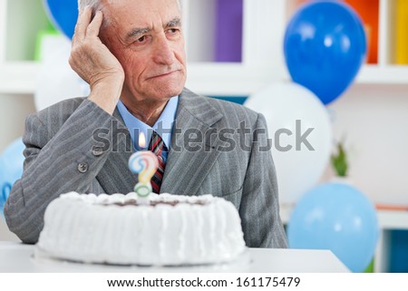 Senior man sitting front of birthday cake and trying to remember how old is