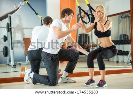 Woman doing workout with fitness straps under supervision an personal trainer