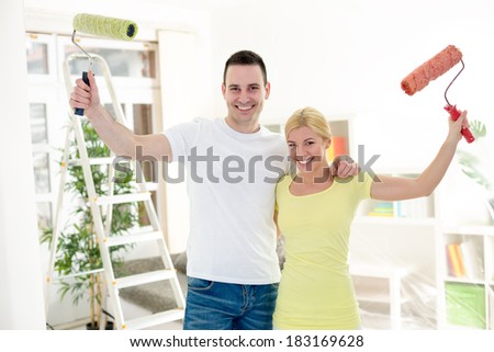 Happy couple holding raised paint roller, concept painting apartment