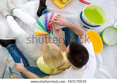 Couple sitting on floor surrounded equipment for painting and chooses a color, top view