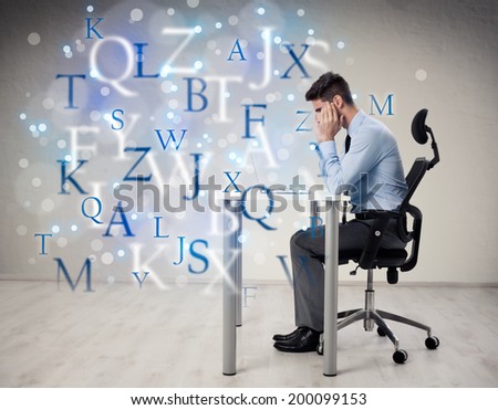young male student sitting at desk and thinking with letters flying around him