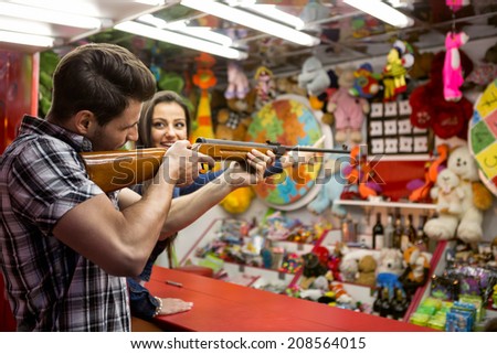 Young fun couple playing shooting games at amusement park