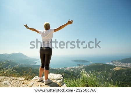 Woman with raised up hands enjoying sunny day,  mountains landscape