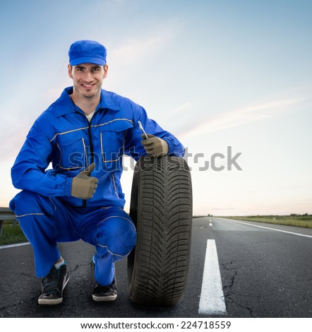 Young Smiling mechanic showing thumbs up next  car tires - road assistance, Towing Service