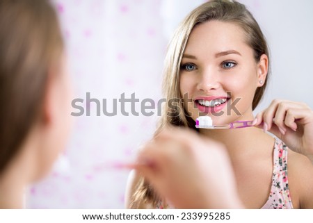 Pretty female looking in mirror while brushing teeth, dental hygiene
