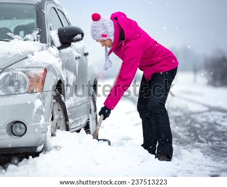 woman shoveling and removing snow from her car, stuck in snow