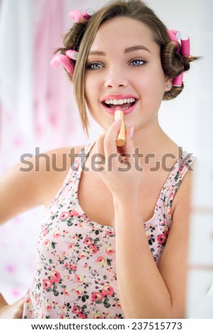 Happy teen girl applying lipstick front mirror