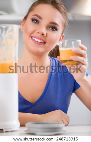 Beautiful woman using a blender while holding a drink in the kitchen