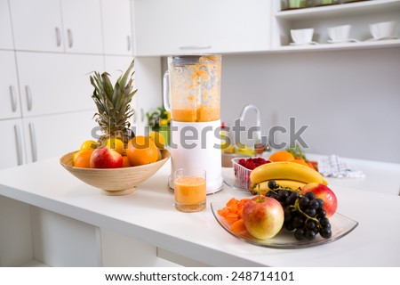 healthy smoothie ingredients in blender with fresh fruit on kitchen table