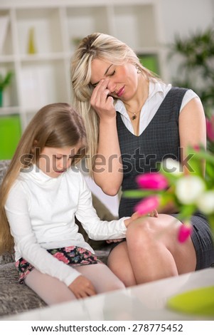 Sad girl sitting on sofa next worried mom at home