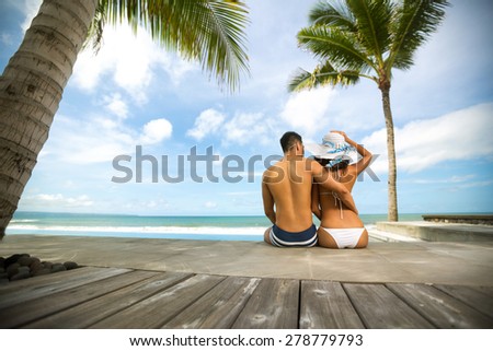 Love couple in tropical resort sitting on sea cost and looking at sea, back view