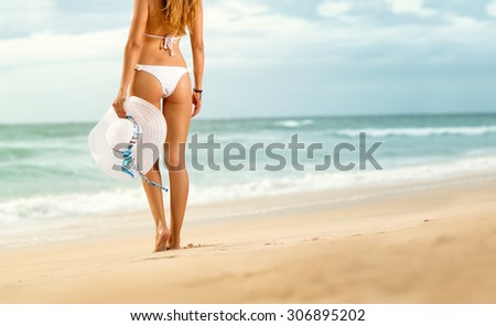 Fit woman standing on beach with hat in hand , back view