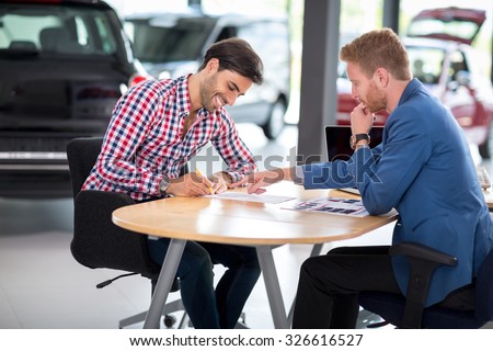 Happy man with car dealer buying a car signs the contract in car showroom