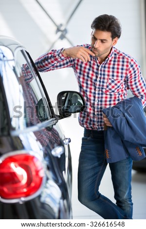 Interested man  examines a new car in showroom, leaning against it watch at the interior of a new car