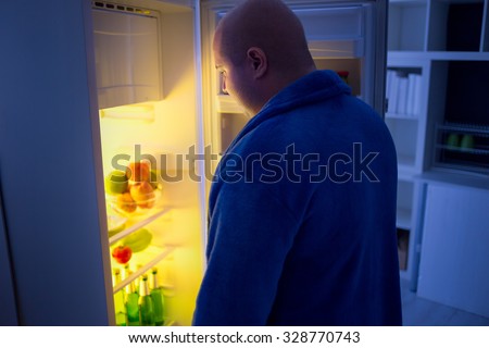 overweight guy at night open refrigerator looking for food