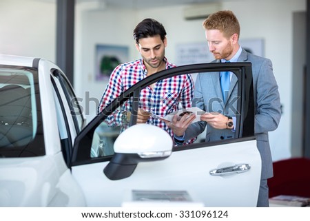 Car salesperson demonstrating a new automobile to young man