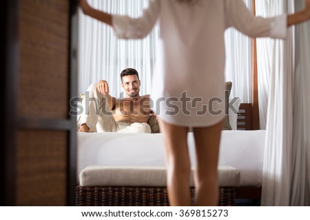 woman seduces her boyfriend in the bedroom, he lying on bed and looking at her