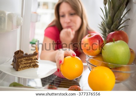 Woman hesitating whether to eat piece of chocolate cake or orange