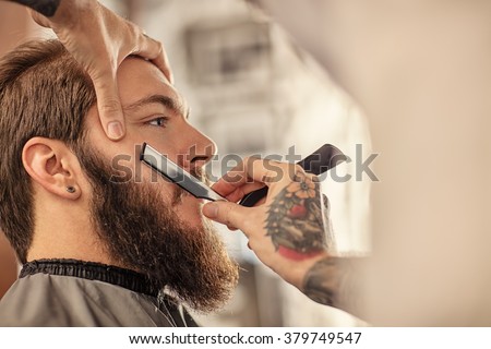 Barber with old-fashioned black razor shaving bearded man