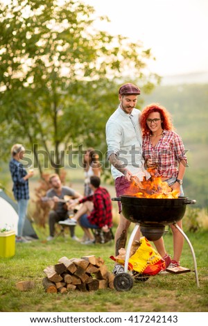 Guy put log on grill fire and hug curly girl in campground