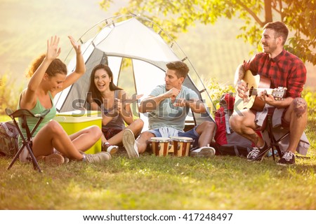 Laughing group of young people enjoy in music of drums and guitar on camping trip