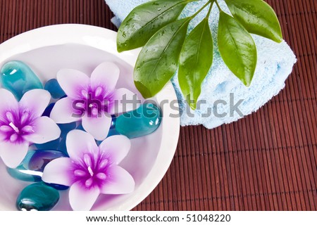 pink flower candles floating in bowl of water beside towel and plant