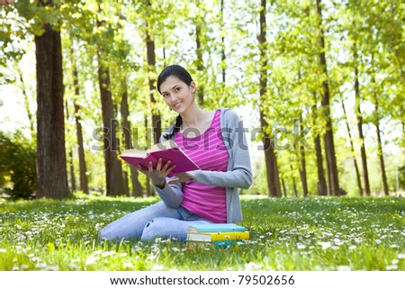 beautiful student enjoying with book in nature, smiling and looking at camera