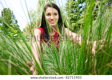 Young  woman  in a field peering through the long grass, looking at camera, horizontal composition