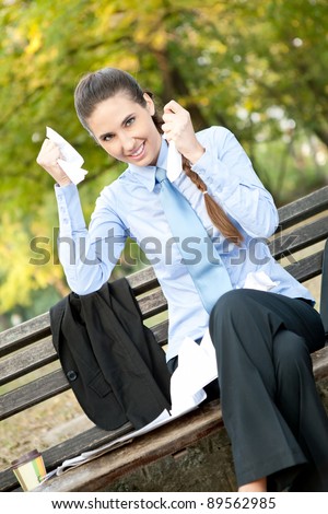 ecstatic businesswoman sitting on bench in park tearing paper , termination of contract