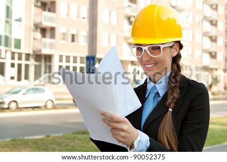smiling female engineer with hard hat reading  blueprints, outdoor
