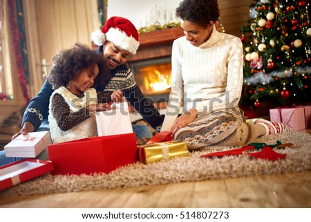 afro American parents looking in their little girl which opens Christmas presents