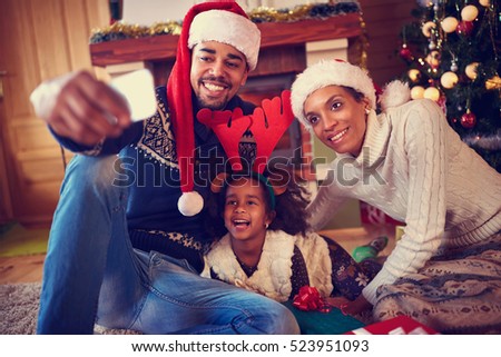 Smiling young family in Christmas atmosphere making photo with smartphone