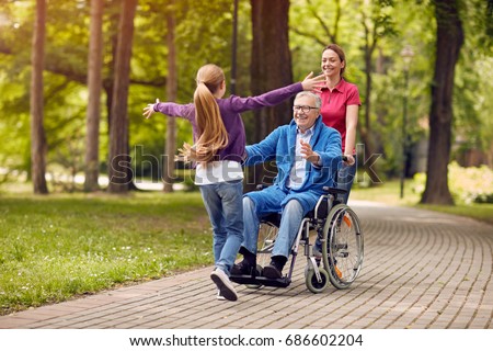 cheerful disabled grandfather in wheelchair welcoming his happy granddaughter