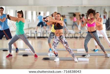 Young group of exercisers doing exercises with resistant rubber in fitness class