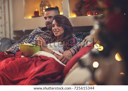 Young man and woman in bed watching tv and eating pop corn
