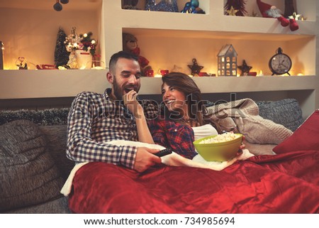 Young Chrismas couple enjoy together looking movie and eat popcorn in bed