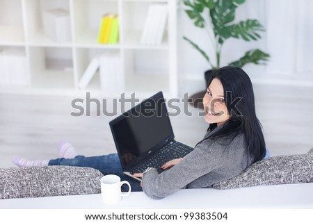 Happy woman at home sitting in front of computer and looking at camera.