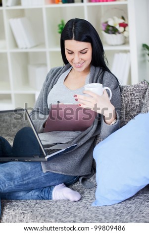 young woman works on the laptop with cup of coffee on a sofa