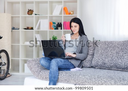 Woman holding a mug while using a laptop in her living room