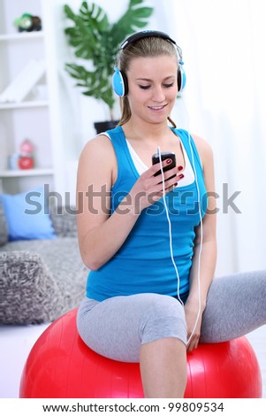 Young girl siting on fit ball and choosing music for exercise, preparing for practice