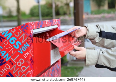 Coquitlam, BC Canada - April 24, 2014 : Hand sending a tax report letter in a red mail box