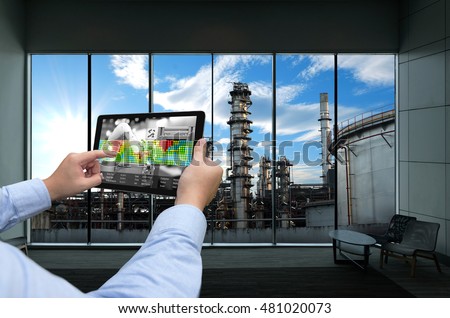 Industry 4.0 concept .Man hand holding tablet with Augmented reality screen and automate wireless Robot arm software at industrial room in smart factory.Window showing oil refinery industry background