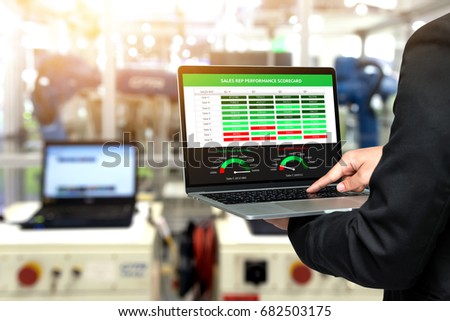Male manager hand suit using laptop with machine real time monitoring sale rep performance scorecard system software. Blur robot arm machine in smart factory. Industry 4th iot , digital manufacturing.
