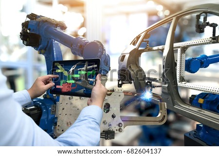 Industry 4.0 concept . Man hand holding tablet with performance check screen software and automate wireless Robot arm in automobile smart factory background.