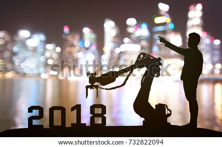 Silhouette of business man command automation robot advisor for 2018 new year technology , industry 4.0 , artificial intelligence  trend concept. Blur Bokeh flare light night building background.